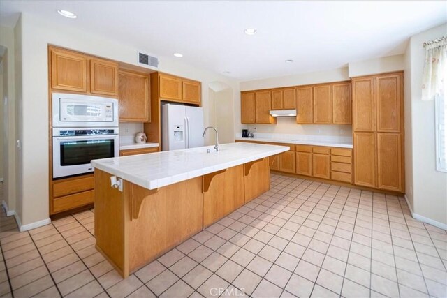 391 Camino Carta, San Marcos, CA 92078 - kitchen with tile countertops, white appliances, visible vents, under cabinet range hood, and light tile patterned flooring