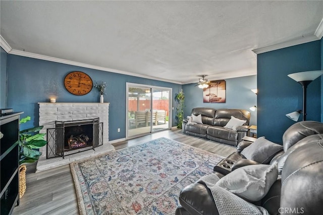 living area with ornamental molding, wood finished floors, a fireplace, baseboards, and ceiling fan