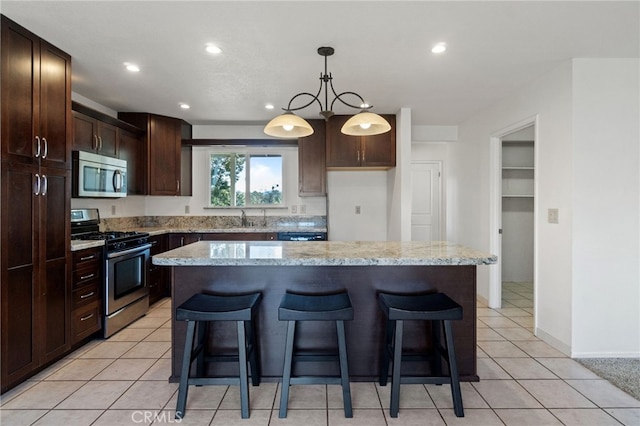 kitchen with a sink, stainless steel appliances, a kitchen bar, decorative light fixtures, and recessed lighting