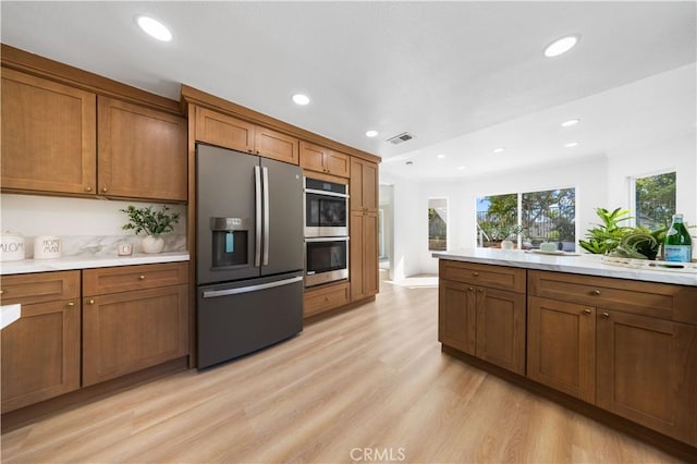 kitchen featuring appliances with stainless steel finishes, brown cabinetry, light wood finished floors, and visible vents