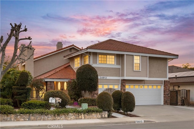 traditional-style house featuring concrete driveway, a tiled roof, stucco siding, and a garage