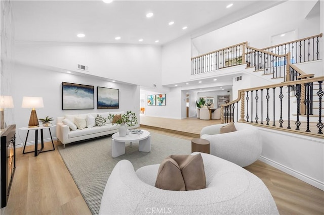 living area with light wood-style floors, baseboards, a towering ceiling, visible vents, and stairway