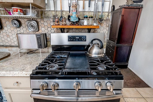 details featuring baseboards, stainless steel range with gas stovetop, decorative backsplash, and fridge