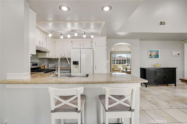 kitchen with a peninsula, stainless steel gas range, white fridge with ice dispenser, arched walkways, and a sink