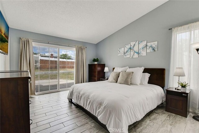 bedroom featuring light wood-style flooring, access to outside, vaulted ceiling, and a textured ceiling