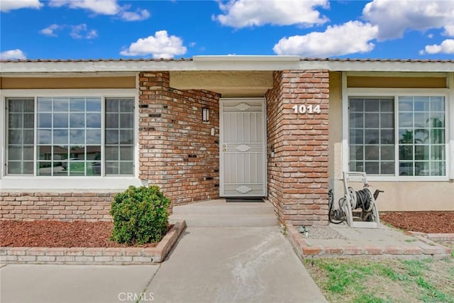 view of exterior entry with metal roof, stucco siding, and brick siding