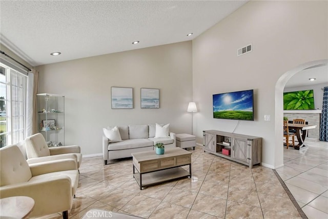 living area featuring lofted ceiling, baseboards, a textured ceiling, arched walkways, and visible vents