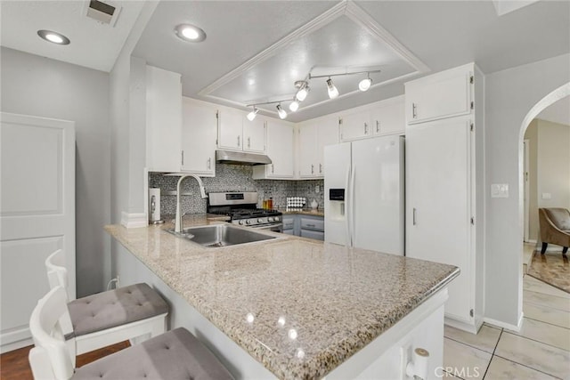 kitchen featuring stainless steel gas range, white fridge with ice dispenser, arched walkways, under cabinet range hood, and a sink