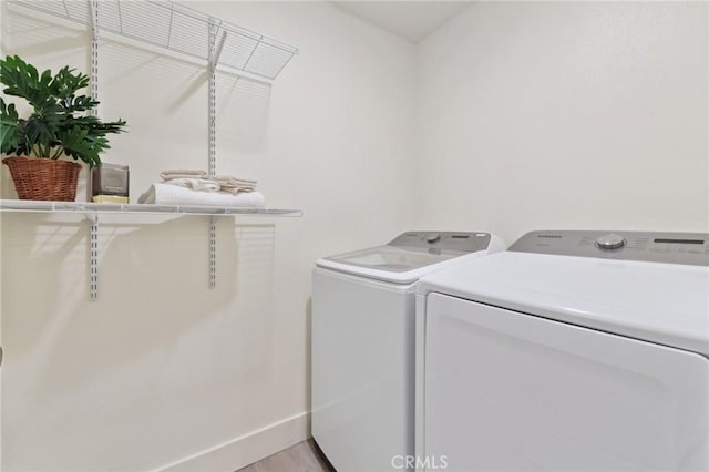 clothes washing area featuring separate washer and dryer, baseboards, light wood-style floors, and laundry area