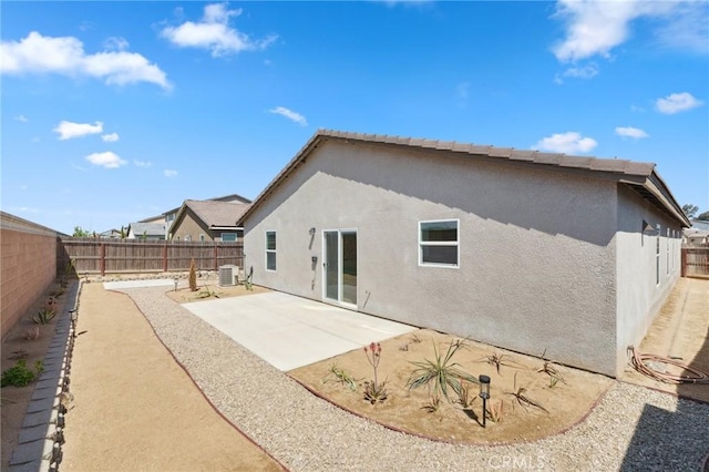 rear view of house with a fenced backyard, cooling unit, stucco siding, and a patio