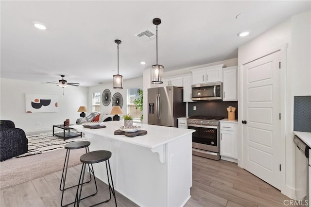 kitchen featuring open floor plan, a kitchen bar, stainless steel appliances, backsplash, and visible vents