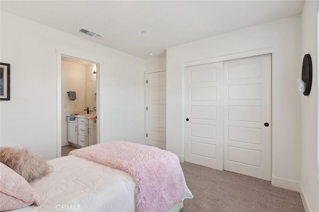 bedroom with a closet, light carpet, ensuite bath, baseboards, and visible vents
