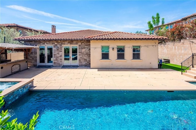 rear view of property with an outdoor pool, stone siding, a tiled roof, french doors, and fence
