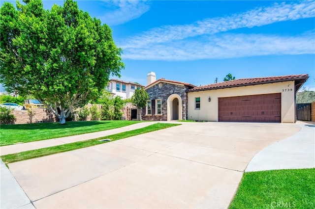 mediterranean / spanish house featuring driveway, stone siding, a tiled roof, stucco siding, and a garage