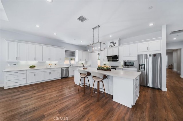 kitchen featuring decorative light fixtures, a kitchen island, light countertops, white cabinets, and appliances with stainless steel finishes