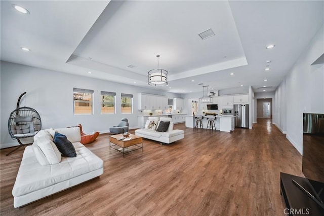 living area with recessed lighting, a tray ceiling, dark wood-style floors, and baseboards