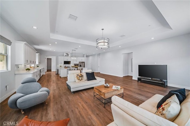 living room featuring recessed lighting, a tray ceiling, visible vents, baseboards, and dark wood finished floors