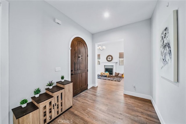 foyer entrance with a fireplace, arched walkways, wood finished floors, and baseboards