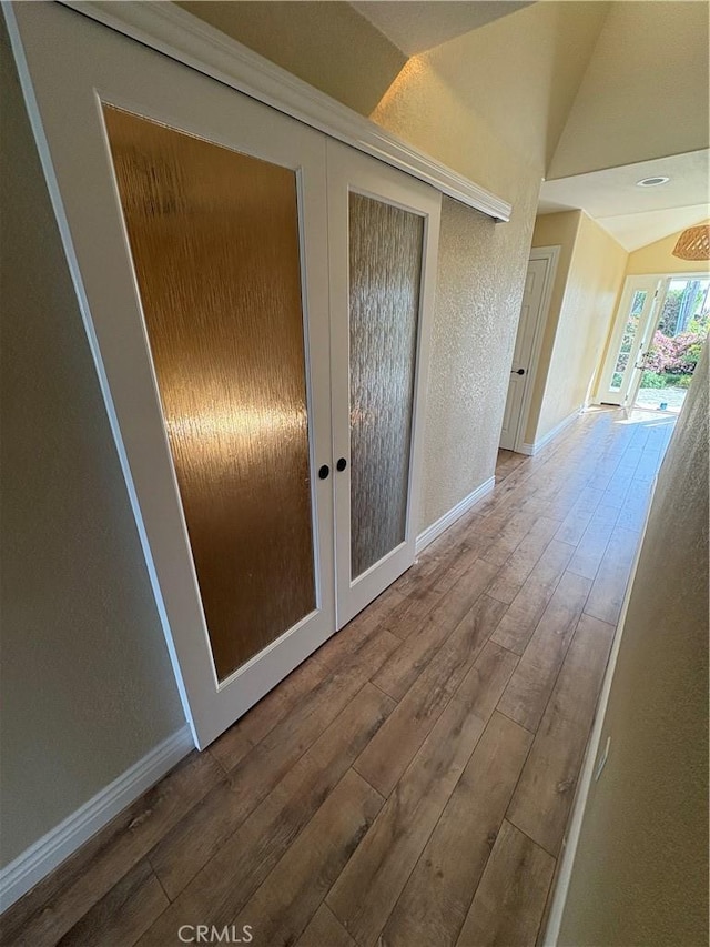hall featuring french doors, vaulted ceiling, baseboards, a textured wall, and hardwood / wood-style flooring