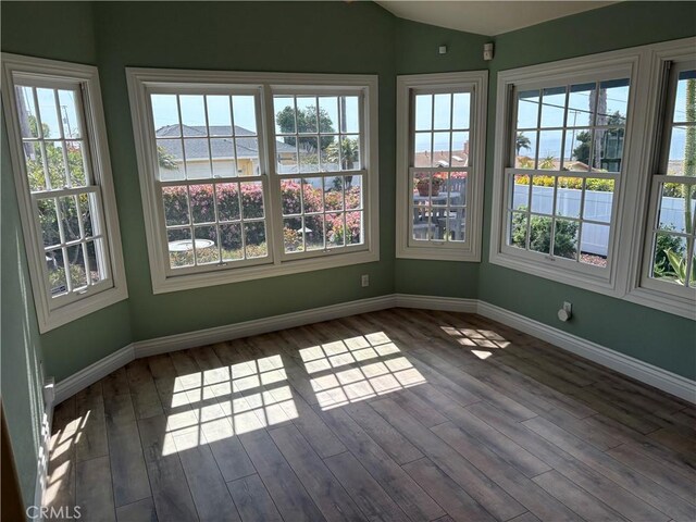 unfurnished sunroom with lofted ceiling, baseboards, wood finished floors, and a healthy amount of sunlight