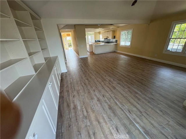 unfurnished living room featuring plenty of natural light, baseboards, and wood finished floors