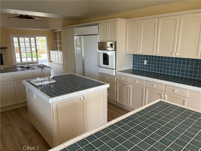 kitchen featuring tile countertops, built in refrigerator, oven, and wood finished floors