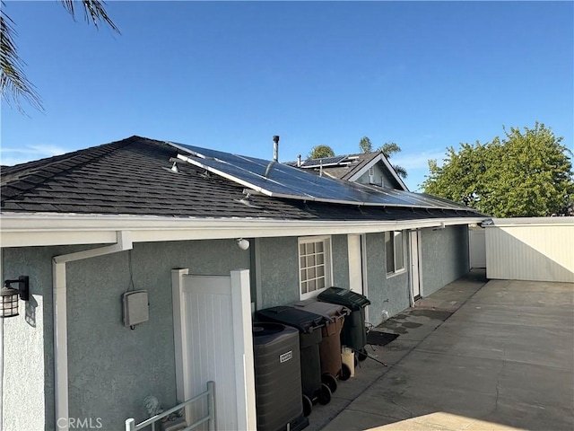 rear view of house featuring solar panels, a shingled roof, fence, and stucco siding