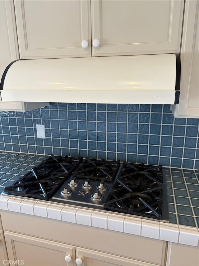 details with tile counters, tasteful backsplash, exhaust hood, and gas cooktop