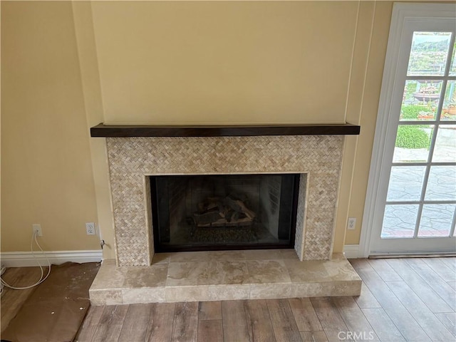 details with baseboards, wood finished floors, and a tiled fireplace