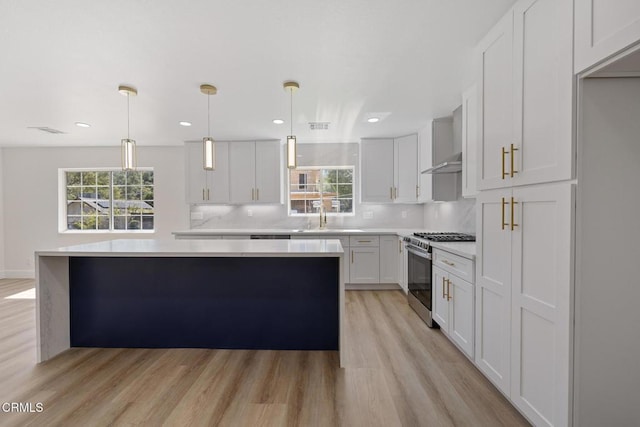 kitchen featuring wall chimney exhaust hood, a healthy amount of sunlight, gas stove, and light countertops