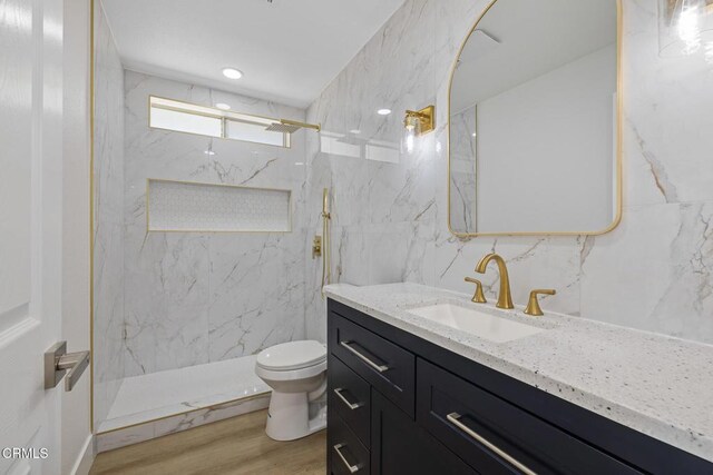 full bath featuring wood finished floors, toilet, vanity, and a marble finish shower