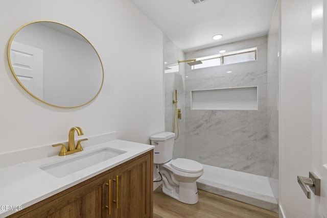 full bath featuring toilet, vanity, wood finished floors, and a marble finish shower