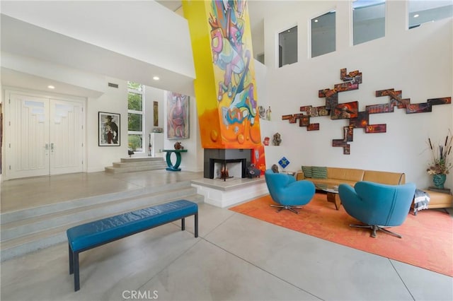 living room featuring visible vents, a fireplace with raised hearth, recessed lighting, a towering ceiling, and finished concrete flooring