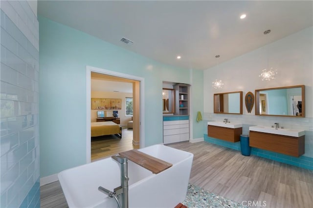 ensuite bathroom featuring a sink, visible vents, a soaking tub, and wood finished floors