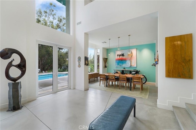 dining area featuring a towering ceiling, visible vents, baseboards, and concrete flooring