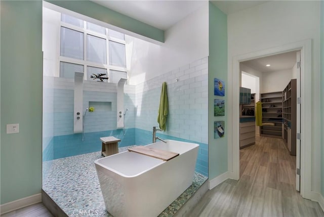 bathroom featuring baseboards, a freestanding tub, a walk in closet, a walk in shower, and wood finished floors