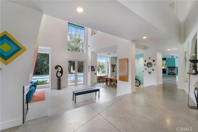 interior space with baseboards, a high ceiling, recessed lighting, finished concrete flooring, and french doors