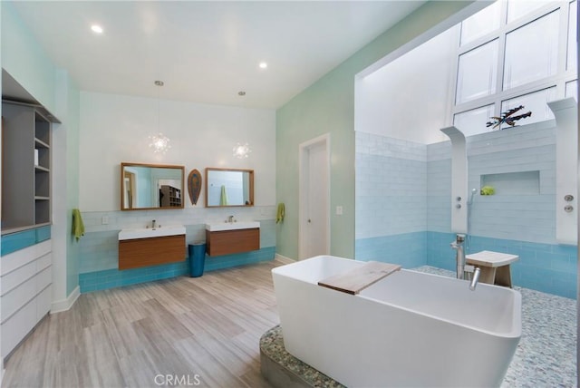 bathroom with a sink, a soaking tub, recessed lighting, wood finished floors, and two vanities