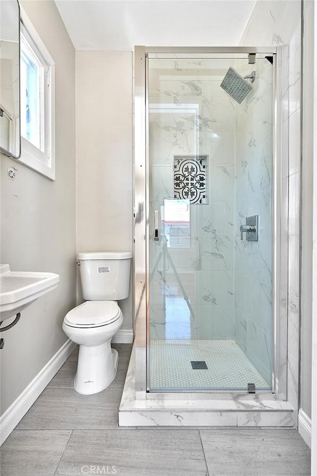 full bath with a marble finish shower, toilet, wood finished floors, and baseboards