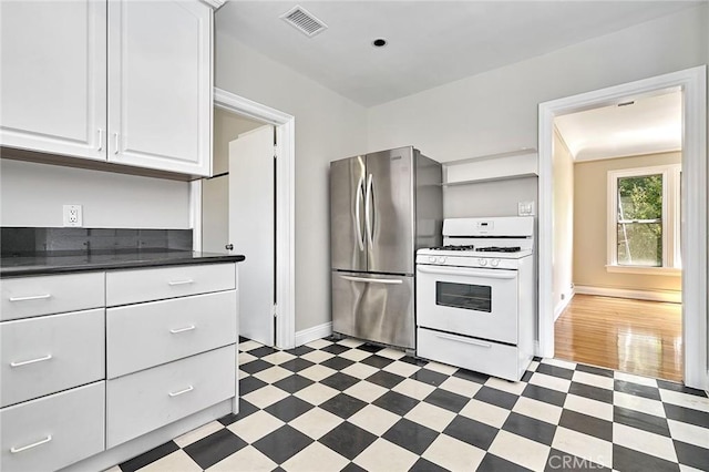 kitchen with visible vents, white cabinets, freestanding refrigerator, white range with gas stovetop, and dark floors