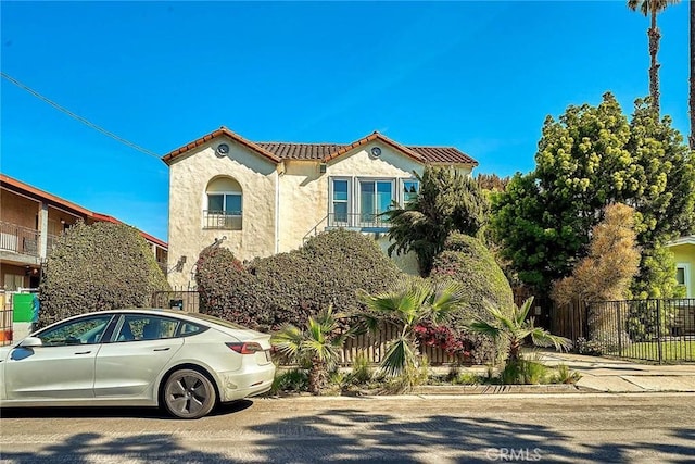 mediterranean / spanish-style home with a tile roof, fence, and stucco siding