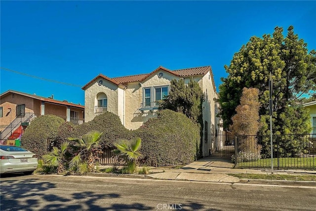 mediterranean / spanish house featuring stucco siding, fence, and a tile roof