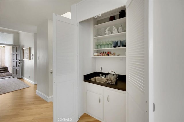 indoor wet bar featuring light wood-style flooring and baseboards