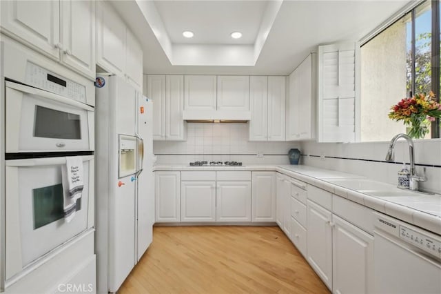 kitchen with white appliances, a sink, white cabinetry, light wood-style floors, and backsplash
