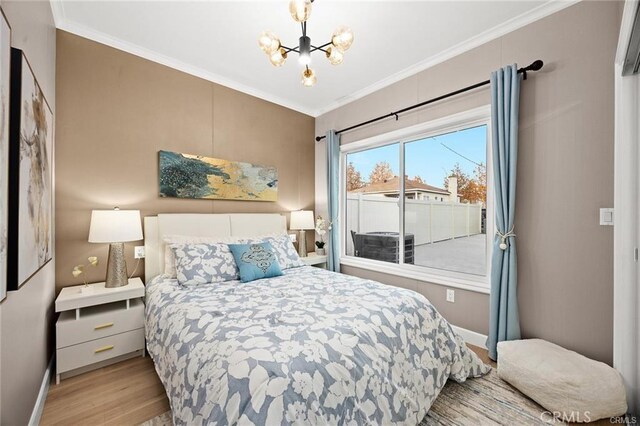 bedroom featuring wood finished floors, ornamental molding, baseboards, and a notable chandelier