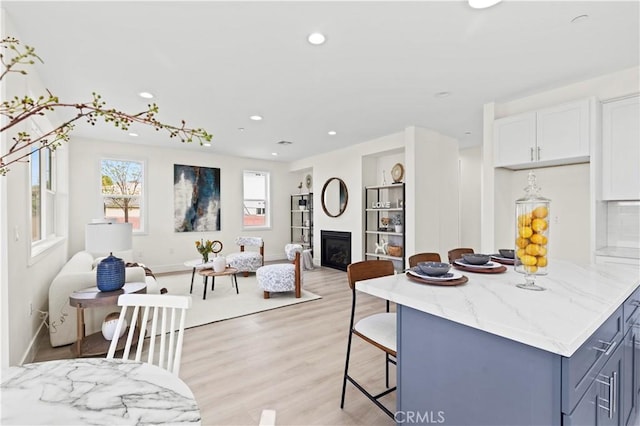kitchen featuring light stone countertops, light wood-style floors, open floor plan, a breakfast bar area, and a glass covered fireplace