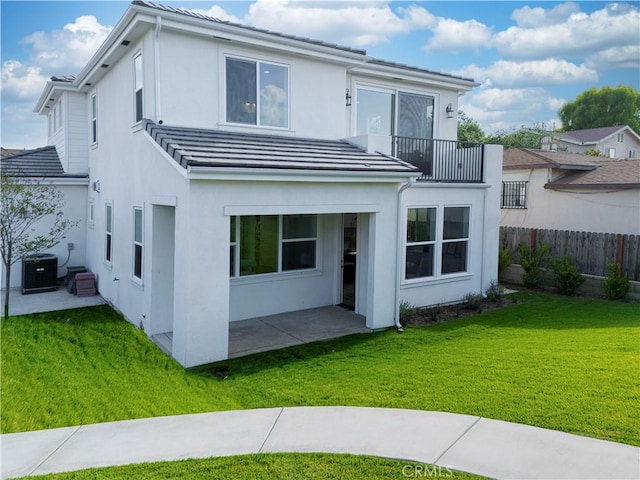 rear view of property with a balcony, central AC unit, fence, a patio, and a yard