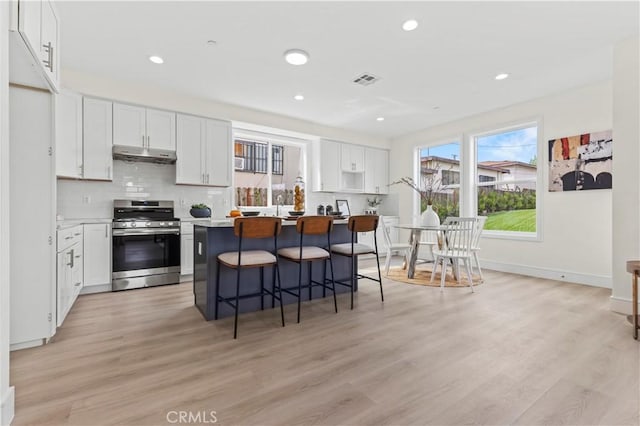 kitchen featuring stainless steel range with gas stovetop, under cabinet range hood, white cabinetry, and a kitchen breakfast bar