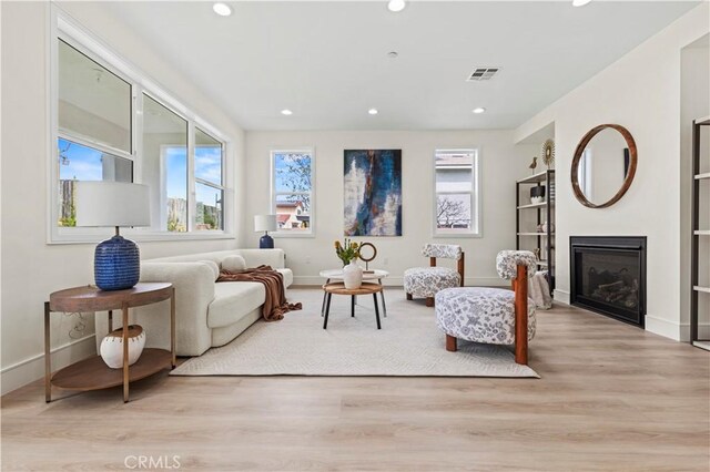 living area featuring light wood finished floors, baseboards, recessed lighting, built in features, and a glass covered fireplace