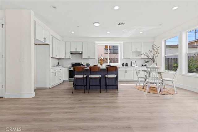 kitchen with visible vents, a kitchen island, white cabinetry, gas range, and a kitchen breakfast bar